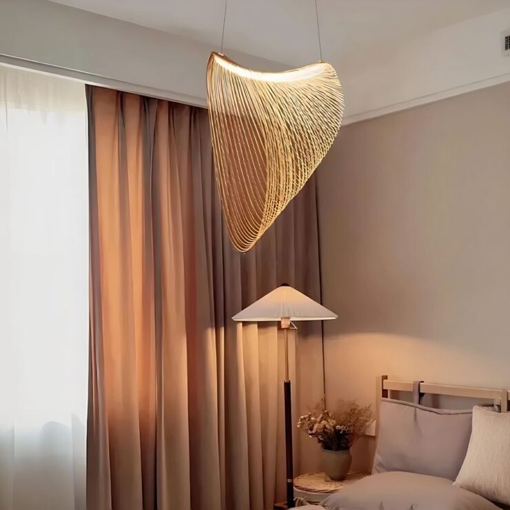 Grand lustre LED avec anneaux en bois suspendus. Deux câbles soutiennent une barre LED allumée. Autour de celle-ci sont suspendus des anneaux en bois du plus petit au plus grand de droite à gauche. Fixé dans une chambre, le mur de droite est marron clair avec un lit à la literie beige. A gauche une grande fenêtre avec un grand rideau marron. Entre le rideau et le lit, une lampe sur pied allumée avec abat-jour en forme de cône.