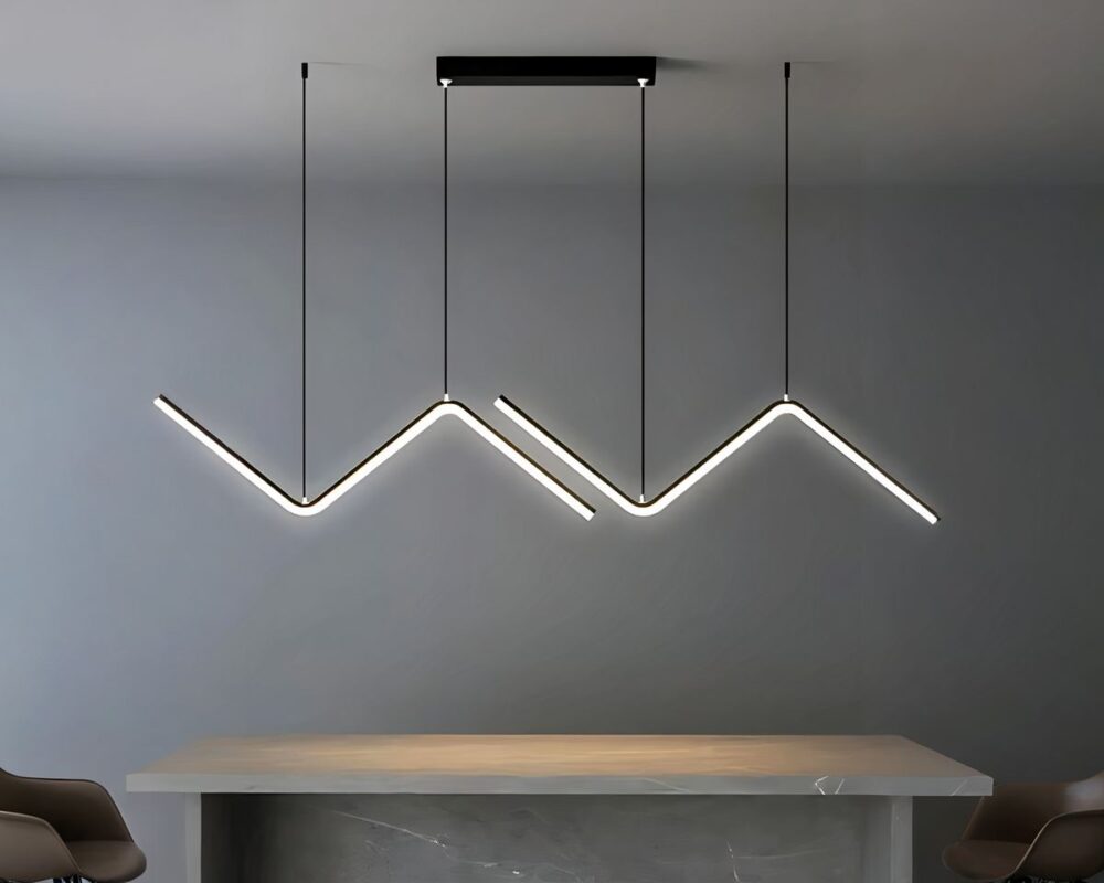 Grand lustre suspendu en deux parties. Au plafond un socle rectangulaire noir auquel sont suspendus deux câbles noirs. Chaque câble est attaché à une ligne géométrique en forme de Z couché noir dont le dessous est une barre de LED allumée. Un deuxième câble de chaque côté tient chaque Z. Dans une pièce aux murs gris, avec une grande table beige sous le lustre.