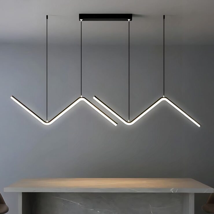 Grand lustre suspendu en deux parties. Au plafond un socle rectangulaire noir auquel sont suspendus deux câbles noirs. Chaque câble est attaché à une ligne géométrique en forme de Z couché noir dont le dessous est une barre de LED allumée. Un deuxième câble de chaque côté tient chaque Z. Dans une pièce aux murs gris, avec une grande table beige sous le lustre.