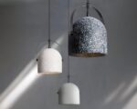 Présentation des trois couleurs de lustres de bureau avec un effet ciment qui sont blanc, noir et gris. Le tout sur un mur gris clair avec des reflet du soleil.