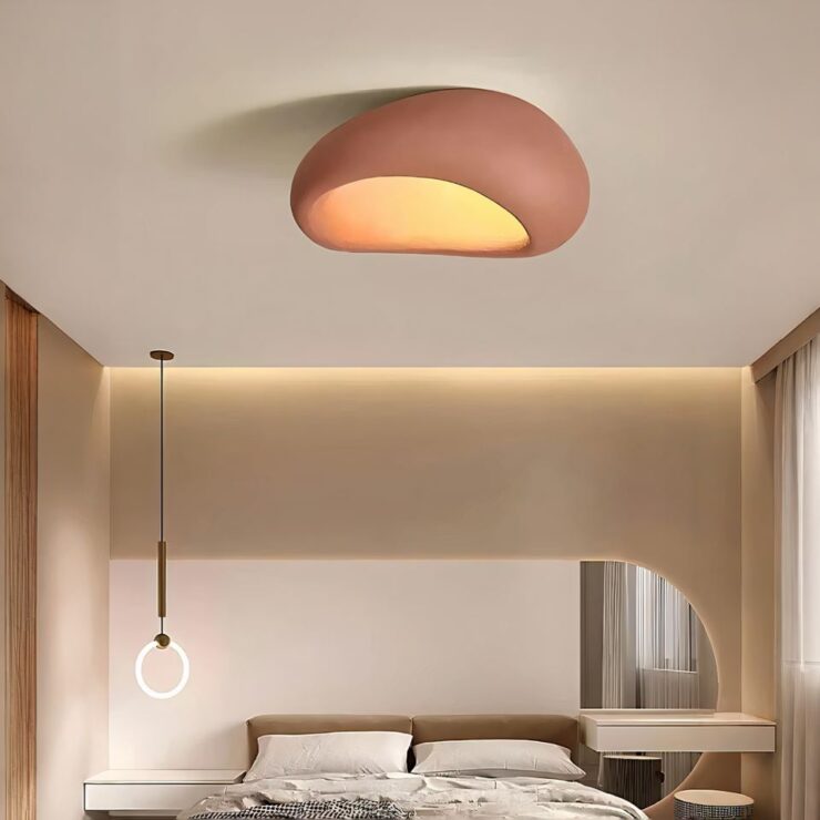 Lustre sans fil au style japonzis wabi-sabi de couleur terracotta fixé sur un plafond beige dans une chambre. Il diffuse une lumière blanc chaud. Au fond de la chambre, on voit un lit 2 place avec une literie blanche. De chaque côté du lit, une table de chevet blanche suspendue. Il y a une fenêtre sur le mur de droite. A gauche du lit, une lampe suspendue avec un anneau lumineux.