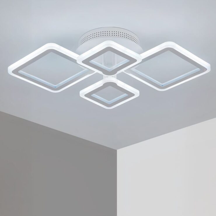 Lustre sans fil avec 4 carrés LED fixé sur un plafond blanc et diffusant une lumière blanc froid. On voit un angle de pièce.