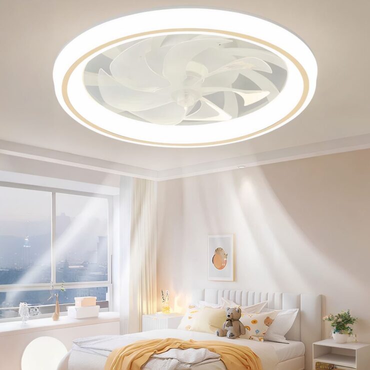 Lustre ventilateur avec anneau lumineux LED sur l'extérieur des pales du ventilateur. Fixé sur un plafond blanc dans une chambre. A gauche une fenêtre sans rideau. A droite un mur beige avec un lit 2 places beige et un linge jaune sur le bout du lit.