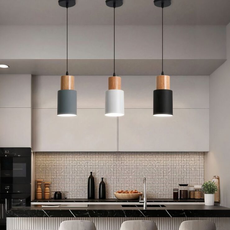 Les petits lustres de chaque couleur : noir,gris et blanc sont installés au-dessus d'un plan de travail central d'une cuisine.