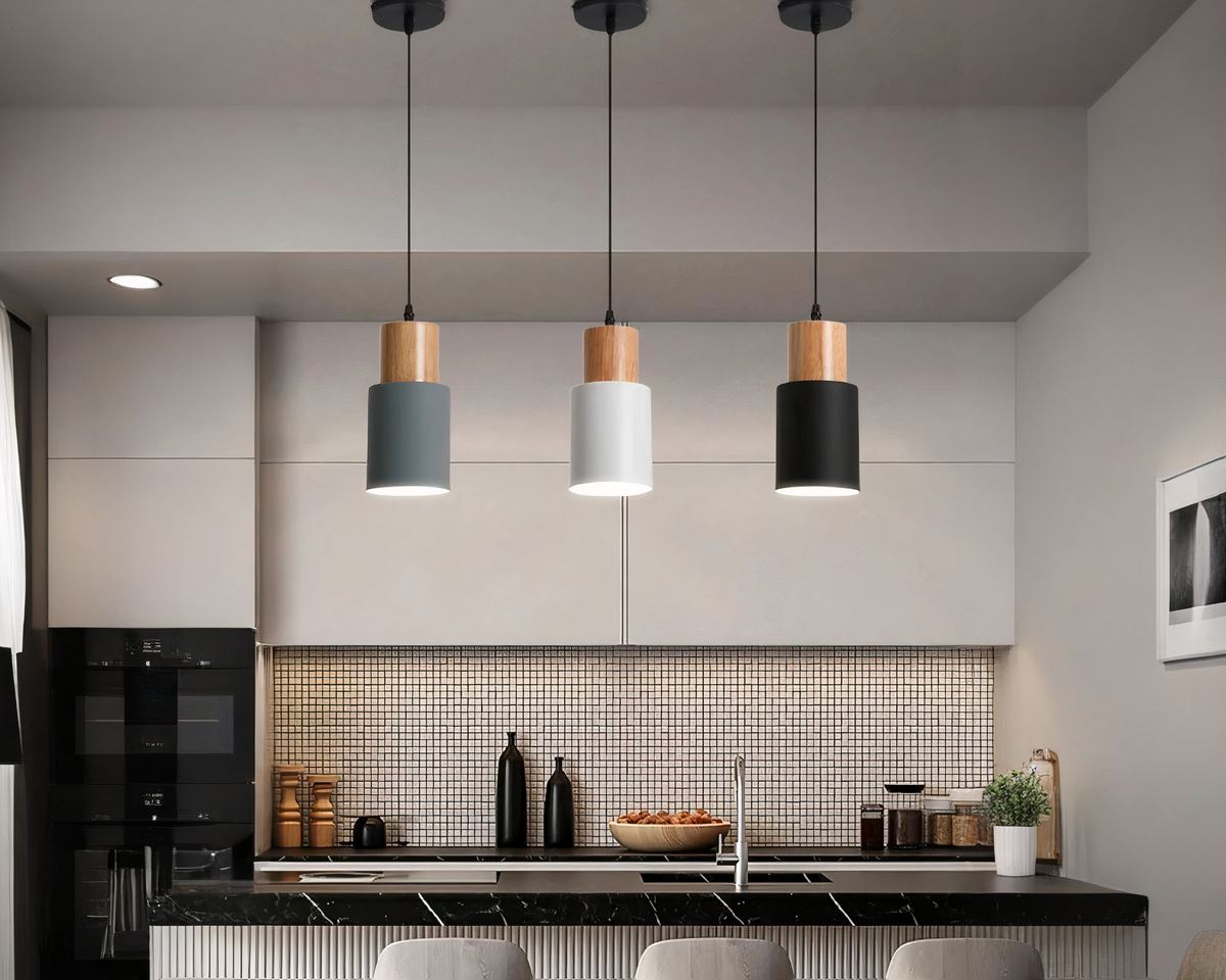 Les petits lustres de chaque couleur : noir,gris et blanc sont installés au-dessus d'un plan de travail central d'une cuisine.