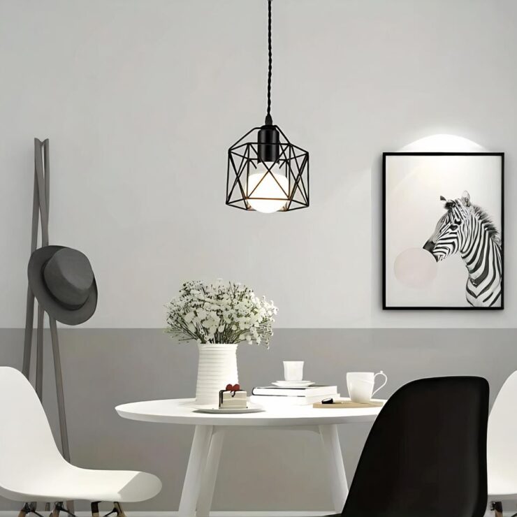 Le petit lustre nordique au style industriel au dessus d'une table blanche avec dans le fond à droite un cadre avec un zebre et à gauche un porte-manteau avec un chapeau dessus.