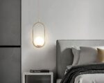 Petit lustre au modèle ovale sur le côté d'un lit sur fond gris
