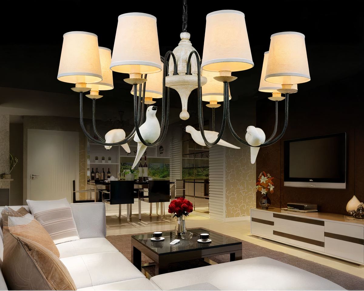 Lustre avec abat-jour romantique et oiseaux perchés, dans sa variante huit abat-jour, suspendu dans un salon, au-dessus d'un canapé blanc et en bois. Le lustre est allumé.