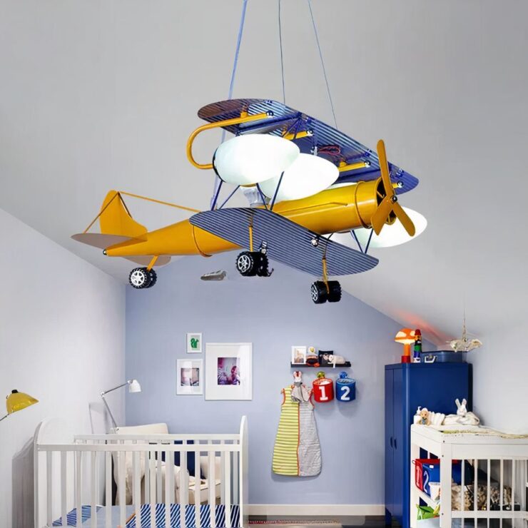 Lustre bébé avion rétro allumé est suspenbdu dans une chambre de bébé. On aperçoit un lit à barreaux ainsi que la table à langer, et le mur du fond est bleu.