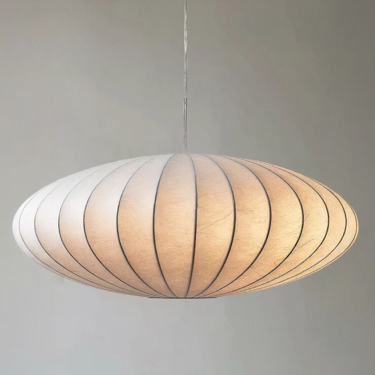 Lustre japonais en soie blanche de forme ovale allongée. Il est suspendu par un câble fin, la lumière est allumée. Sur fond gris.