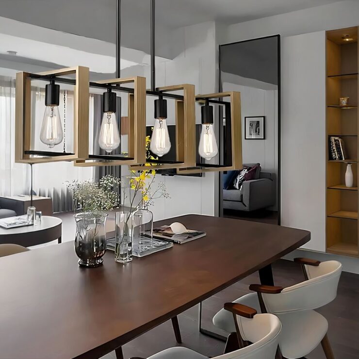 On voit une pièce avec un grande table rectangulaire en bois avec des pieds noirs. A droite de la table, deux sièges blancs. Sur la table, des vases transparents avec des fleurs fines et des magazines. A droite de la table, un mur avec un miroir sur toute la hauteur et à droite des étagères intégrées au mur. Au-dessus de la table, un lustre campagne suspendu aux lignes géométriques. Un rectangle noir soutenant 4 ampoules allumées, qui lui-même est suspendu par deux tiges noires. Dans la perpendiculaire du rectangle noir, quatre carrés en bois au niveau de chaque ampoule.