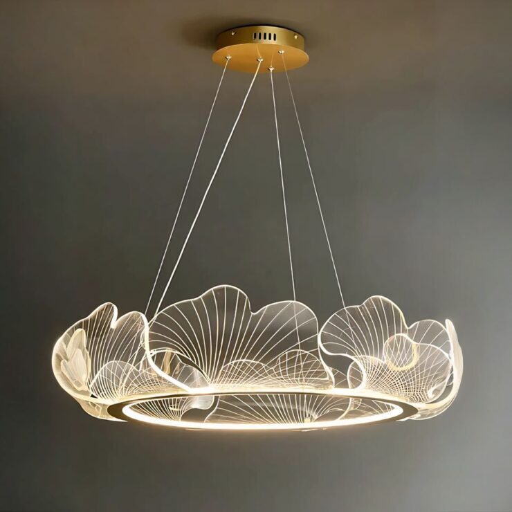 Lustre chic suspendu en acrylique en forme de cercle. Le cercle en acrylique représente des motifs de feuilles. Il est suspendu par des câbles fins fixé sur un rond doré au plafond. Le fond est gris.