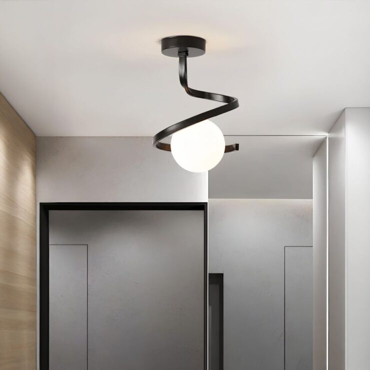 Lustre d'entrée spirale avec boule lumineuse fixé sur un plafond blanc. La spirale est en métal noir et la boule lumineuse se trouve au centre. Sur la gauche, un mur marron, sur la droite un mur blanc. En face, un mur avec un grand miroir sur la droite et une porte à gauche.