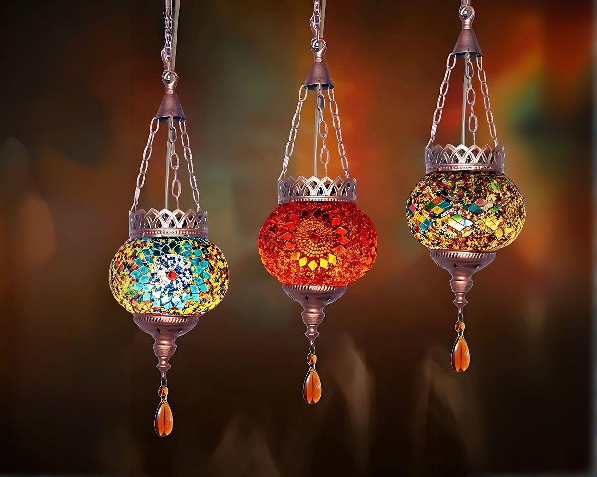 3 Lustres marocains avec lanterne colorée suspendue par une chaîne en métal au bout desquelles on trouve une couronne en métal sous laquelle se trouve un globe en mosaïque ( jaune et vert à gauche, rouge orangé au centre et jaune et marron à droite). Sous chaque globe se trouve suspendue une goutte en métal. Le fond est coloré en dégradé.