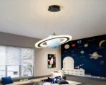 Un lustre suspendu représentant une planète bleue avec un anneau lumineux autour d'elle. Il est accroché au plafond d'une chambre d'enfant décorée sur le thème de l'espace.