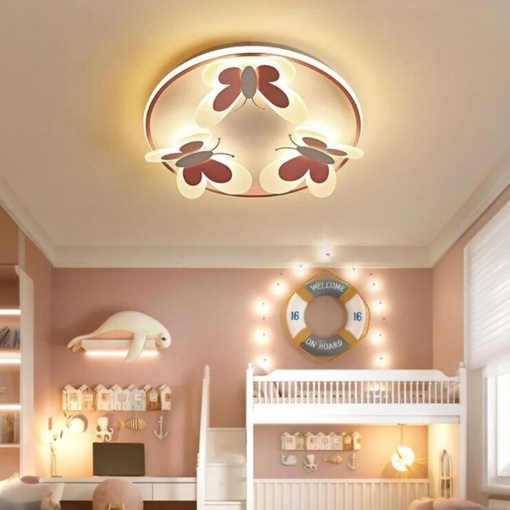 Un lustre chambre fille plafonnier papillon lumineux de forme ronde et de couleur rose diffuse une lumière douce dans une chambre d'enfant aux tons roses, avec des éléments de décoration marins comme une bouée et une tortue murale.