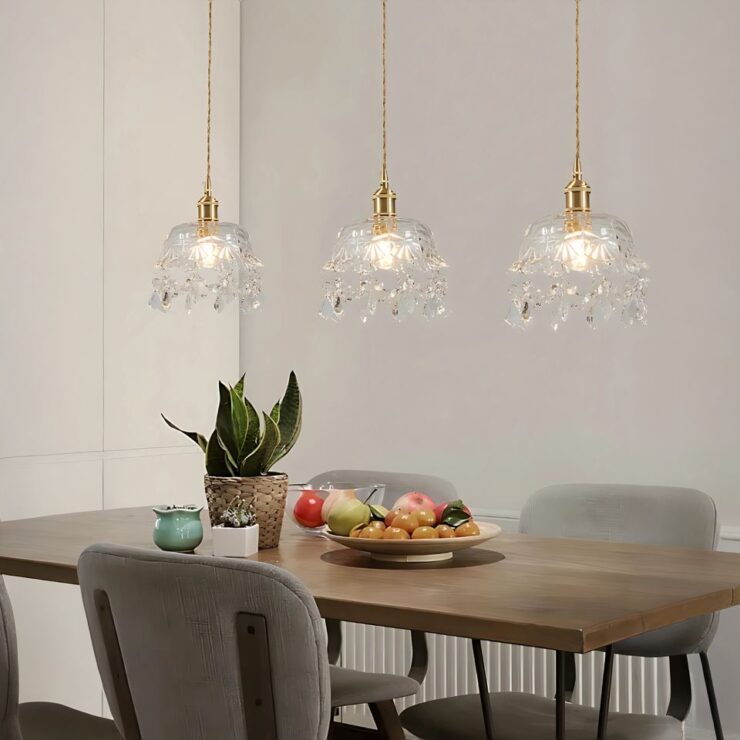 Trois lustres baroque en cristal et fer forgé doré sont alignées au-dessus d'une table à manger en bois. Les cristaux suspendus reflètent la lumière, créant une ambiance élégante et raffinée.