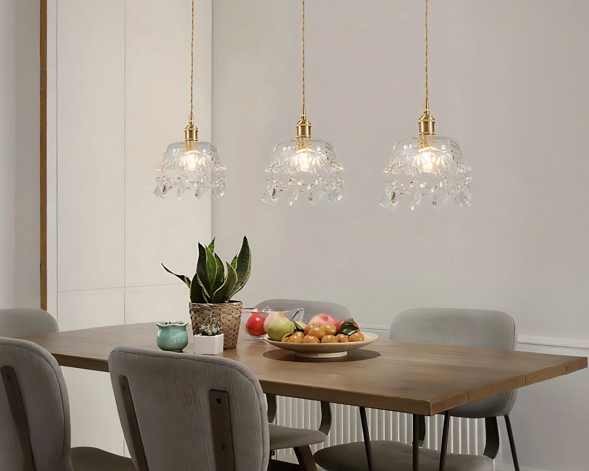 Trois lustres baroque en cristal et fer forgé doré sont alignées au-dessus d'une table à manger en bois. Les cristaux suspendus reflètent la lumière, créant une ambiance élégante et raffinée.