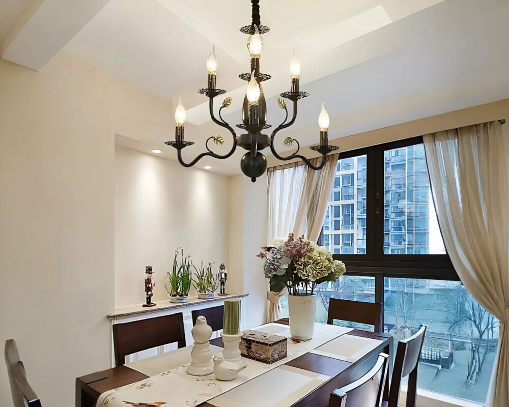 Un lustre baroque majestueux en fer forgé noir imposant, suspendu au plafond, possède plusieurs bras courbés décorés de 6 bougies LED. Il est installé au-dessus d'une table à manger élégante, dans une pièce lumineuse avec une grande fenêtre.