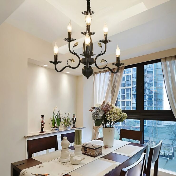 Un lustre baroque majestueux en fer forgé noir imposant, suspendu au plafond, possède plusieurs bras courbés décorés de 6 bougies LED. Il est installé au-dessus d'une table à manger élégante, dans une pièce lumineuse avec une grande fenêtre.