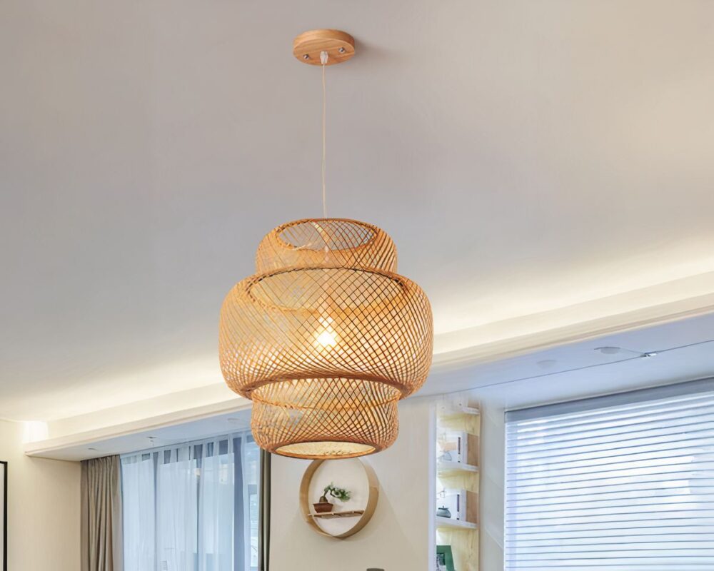 Lustre bohème bambou avec un design à deux niveaux, formé de bandes entrelacées créant une structure ajourée. Le luminaire émet une lumière douce et naturelle. Il est suspendu au plafond par un câble fin avec un socle en bois.