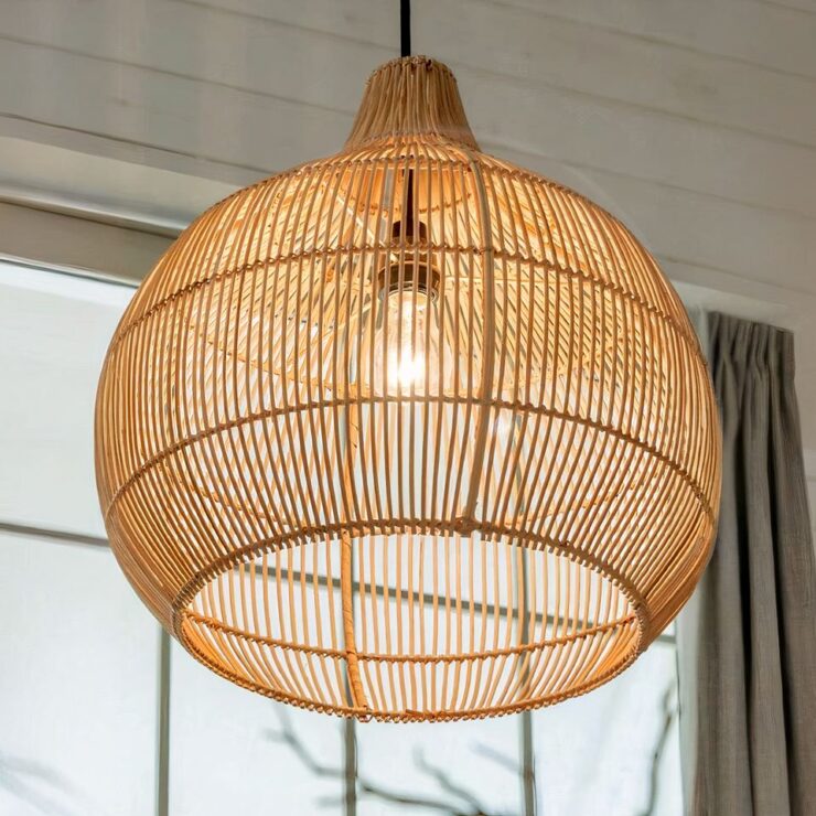 Un lustre bohème en rotin tissé d'une forme arrondie est suspendu. La lumière passe à travers les interstices des tiges fines de rotin, créant un éclairage doux et naturel.
