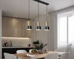 Un Lustre cuisine minimaliste en métal noir et doré est suspendu avec trois suspensions alignées au design moderne et épuré. Il est au-dessus d’une table à manger dans une cuisine moderne.