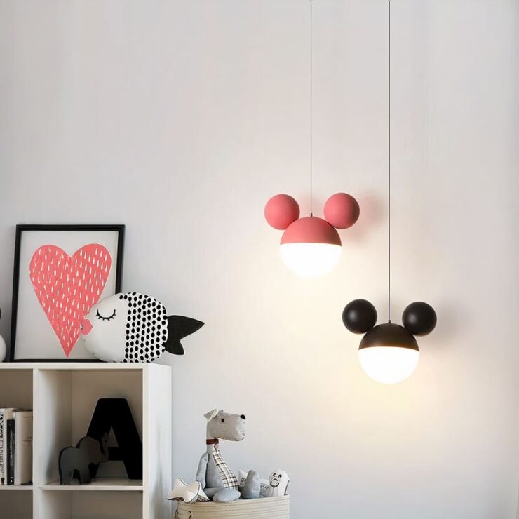 Deux lustres enfant au design de Mickey, l'un rose et l'autre noire, sont accrochés au plafond. Chacun se compose d'une sphère lumineuse avec deux petites sphères au-dessus, représentant les oreilles du célèbre personnage. Ils apportent une touche ludique à une chambre d'enfant décorée avec des peluches et une illustration en forme de cœur.
