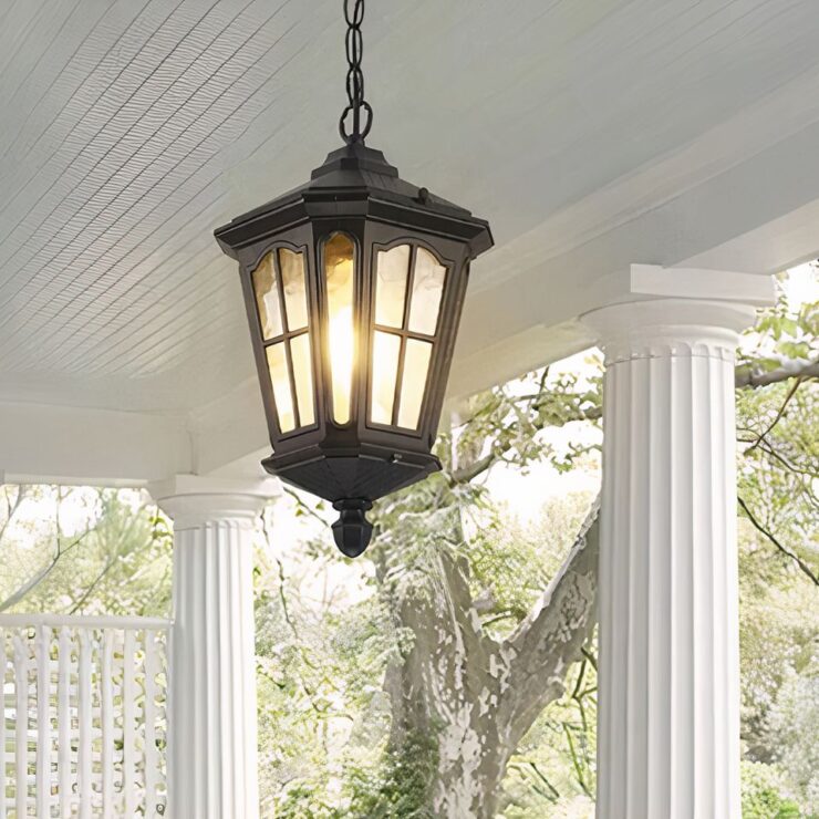 Un lustre extérieur pour terrasse de style rétro en fer forgé est suspendu sous un plafond. Il émet une lumière douce. La suspension est fixée à une chaîne ajustable, créant une ambiance élégante et vintage sur une terrasse couverte.