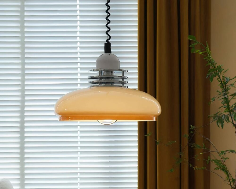 Un lustre opaline beige style rétro avec un design arrondi et des détails métalliques au sommet. Il est accroché par un câble torsadé noir dans une pièce avec des rideaux jaunes et des stores en arrière-plan.