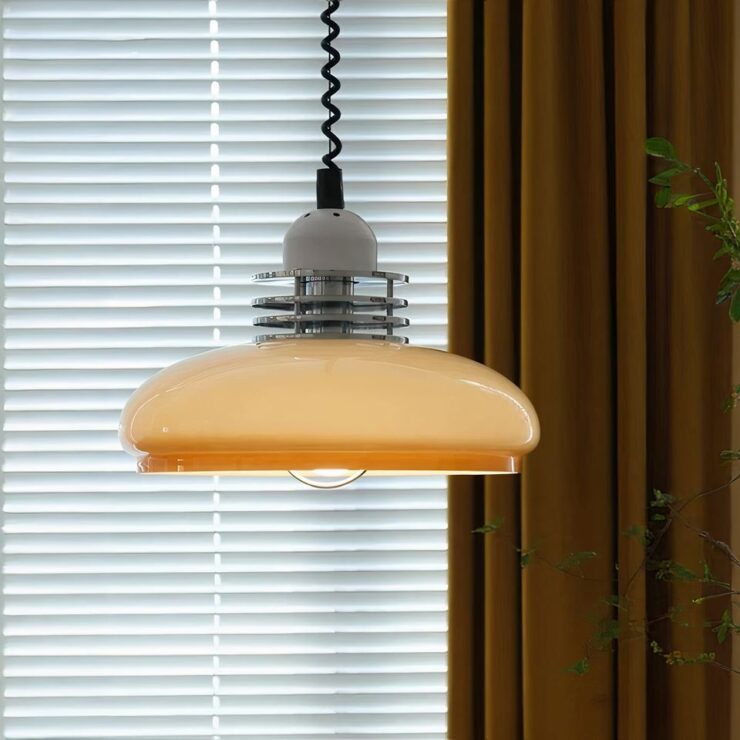 Un lustre opaline beige style rétro avec un design arrondi et des détails métalliques au sommet. Il est accroché par un câble torsadé noir dans une pièce avec des rideaux jaunes et des stores en arrière-plan.