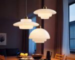 Trois lustres opaline blanc aux courbes raffinées sont suspendus au-dessus d'une table à manger, créant une atmosphère chaleureuse et raffinée dans une pièce tamisée.