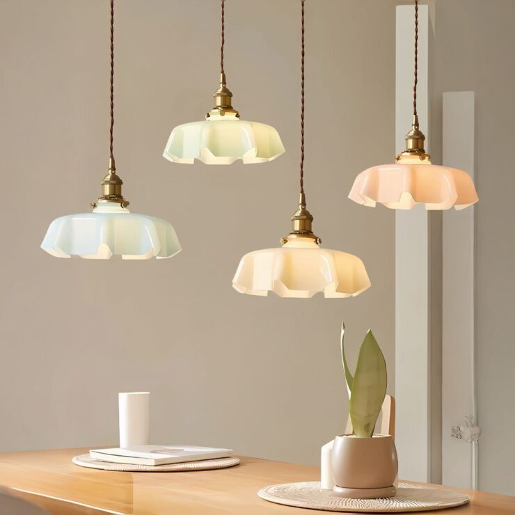 Quatre lustres opaline pastel à bord ondulé sont accrochés par des câbles torsadés marron, créant une ambiance douce et chaleureuse au-dessus d'une table en bois.