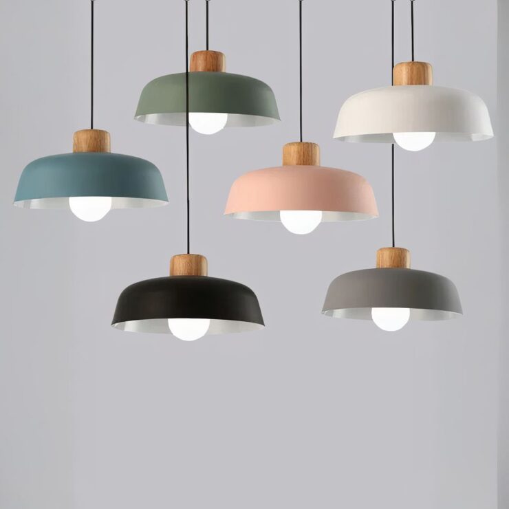 Lustres scandinaves avec abat-jour en métal dans des teintes variées : vert, bleu, rose, noir, gris et blanc. Chaque lustre est suspendu par un câble noir et possède un support en bois, avec une ampoule apparente en dessous.