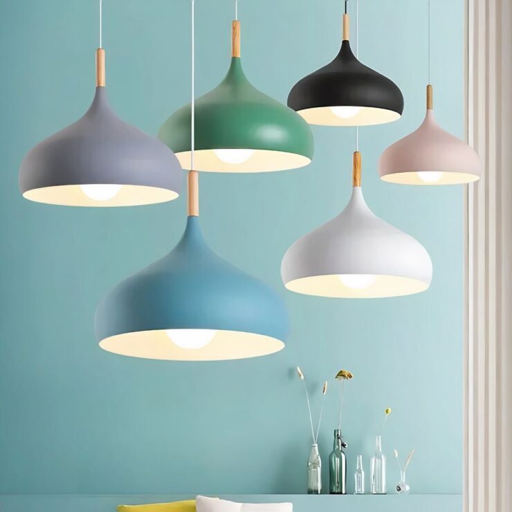 Six lustres scandinave en forme de dôme dans différentes couleurs pastel, dont bleu, vert, gris, noir, blanc et rose. Chaque luminaire a une finition mate avec une tige en bois, suspendu dans un intérieur moderne avec un mur bleu clair.
