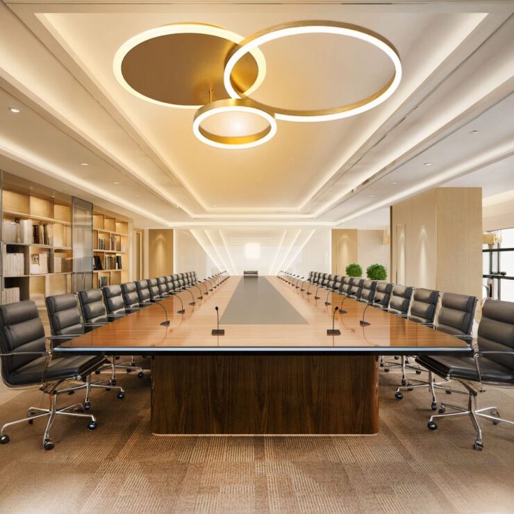 Lustre bureau cercles lumineux en version doré et installé au-dessus d'une grande table de bureau avec des chaises de travail à roulettes rangées.