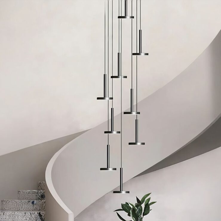 Lustre cage d'escalier moderne et design minimaliste suspendu devant un très bel escalier au garde-corps qui semble etre un genre de pierre naturelle. Le mur est texturé et de couleur beige très clair.