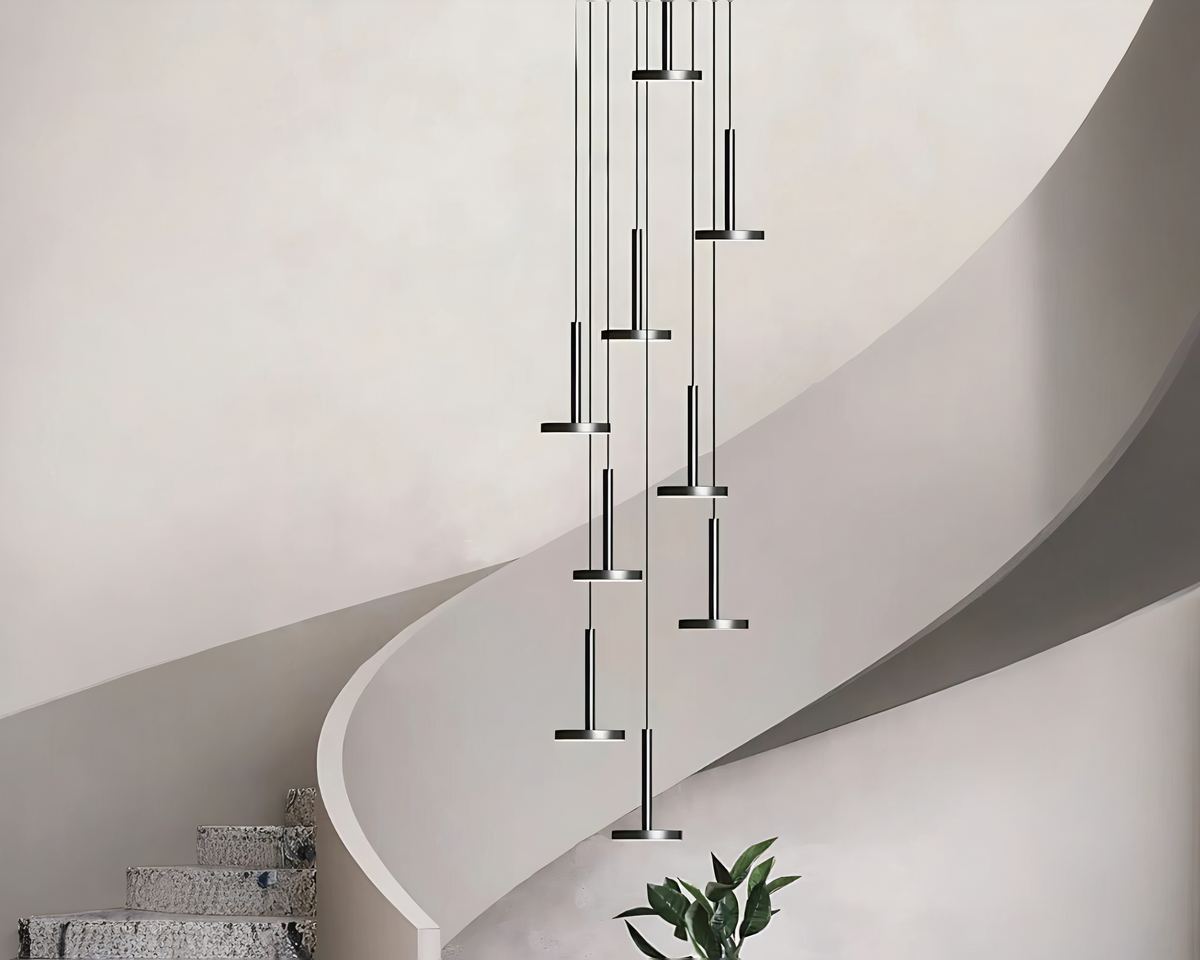 Lustre cage d'escalier moderne et design minimaliste suspendu devant un très bel escalier au garde-corps qui semble etre un genre de pierre naturelle. Le mur est texturé et de couleur beige très clair.