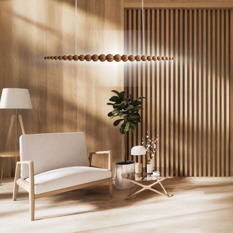 Lustre pendant bois design original multibille, dans sa version bois clair, suspendu au-dessus d'un fauteuil deux places beige avec une plante verte à sa gauche et un lampadaire à l'arrière. Le lustre est allumé.