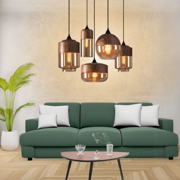 Lustre pendant bois et verre fumé suspendu au-dessus d'un canapé vert et allumé.