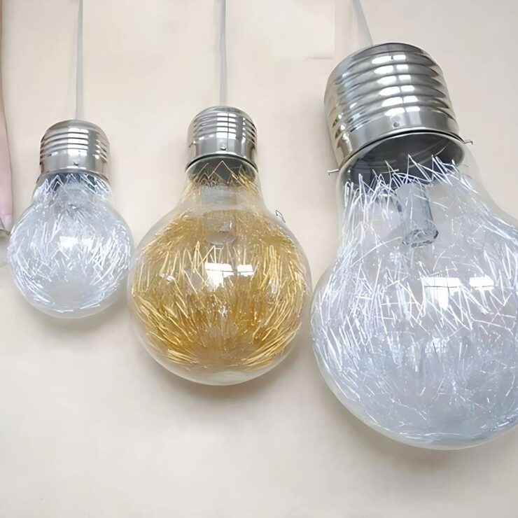 Lustre en forme d'ampoule géante disponible en versions dorées ou argentées et différentes tailles, avec des filaments décoratifs à l'intérieur, créant un effet lumineux étincelant pour une touche élégante et moderne.