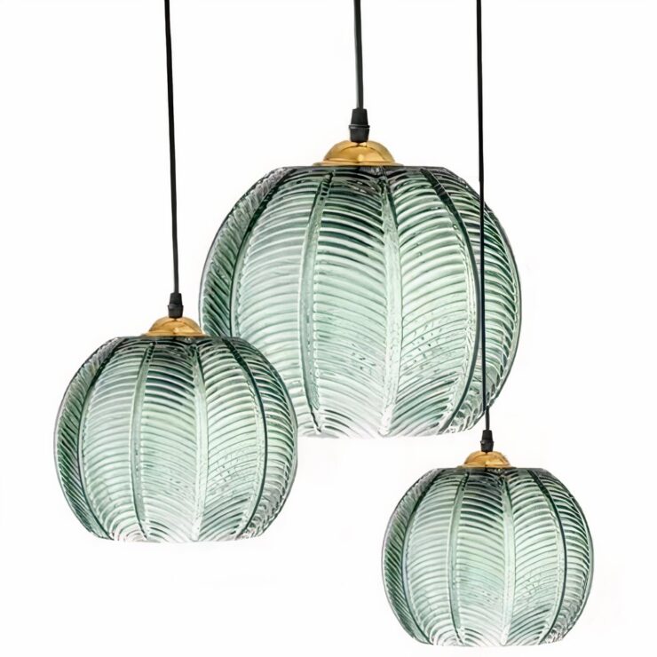 Trois suspensions en forme de boule en verre vert esprit jungle, avec des motifs de feuilles, suspendues par des fils noirs sur fond blanc.
