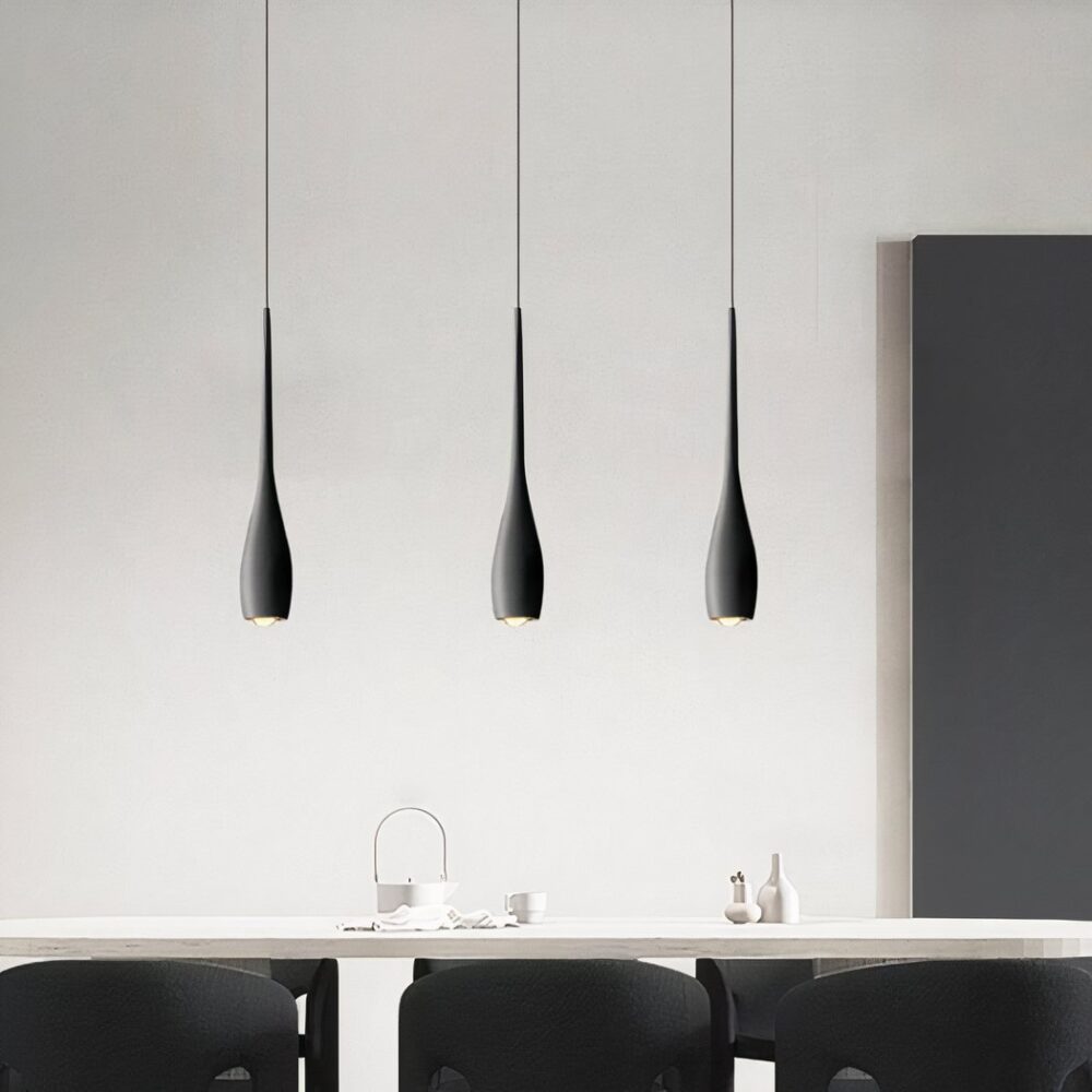 Un lustre suspendu forme goutte design contemporain avec trois suspensions noires fines, au-dessus d’une table dans une pièce moderne et épurée.