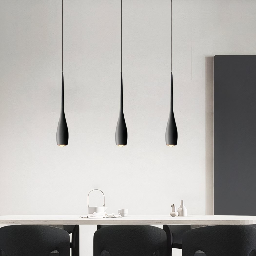 Un lustre suspendu forme goutte design contemporain avec trois suspensions noires fines, au-dessus d’une table dans une pièce moderne et épurée.