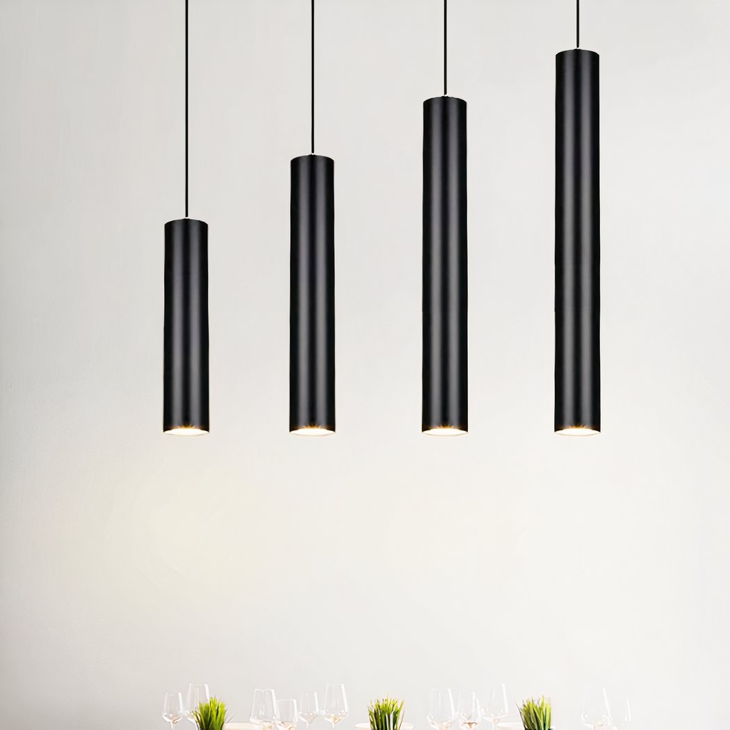 Quatre suspensions tube verticale design épuré moderne noires, longues et fines, pendent au plafond dans une pièce lumineuse au mur blanc.