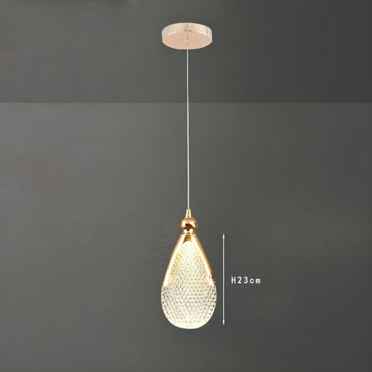 Un lustre goutte d’eau en acrylique doré suspendu au plafond, avec une forme de goutte brillante et un fond gris simple.