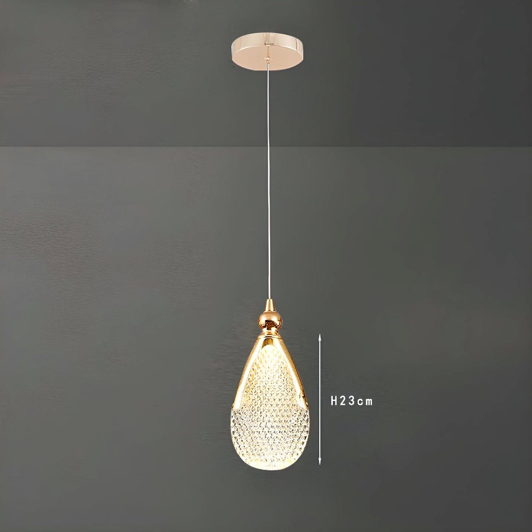 Un lustre goutte d’eau en acrylique doré suspendu au plafond, avec une forme de goutte brillante et un fond gris simple.