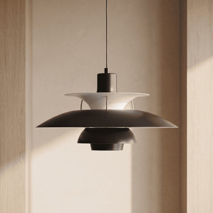 Plusieurs suspension design danois à abat-jour multicouches colorées pendent au-dessus d'une grande table en bois, dans une pièce au mur gris.
